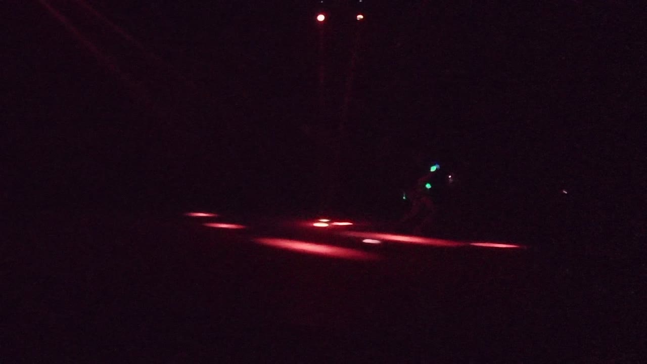 At 0:00 in San Jose del Cabo, a dark stage is crossed by red floor lighting while a faint performer shape stands near the left side of the frame.