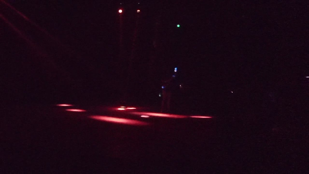 At 0:02 in San Jose del Cabo, the performer is mostly lost in darkness while red floor lights and small green and blue points mark the stage space.