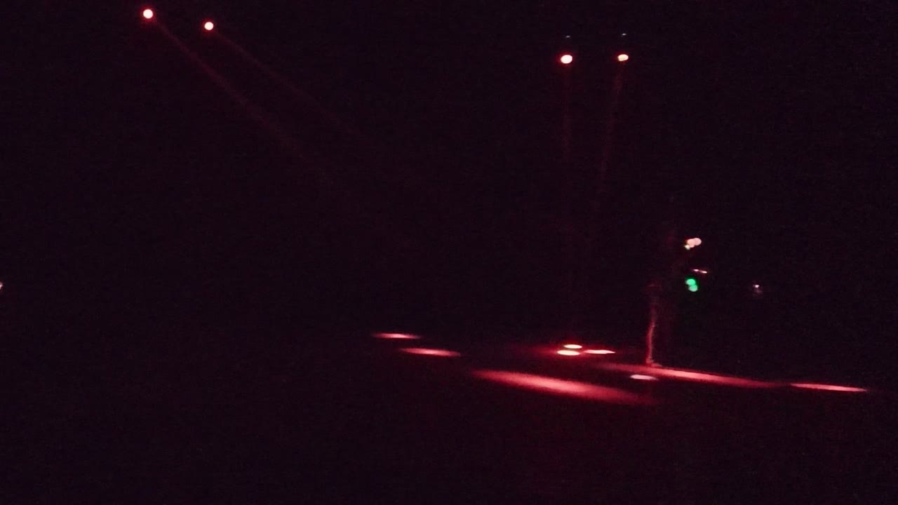 Performer on a dark stage beside red light streaks and small colored lights.