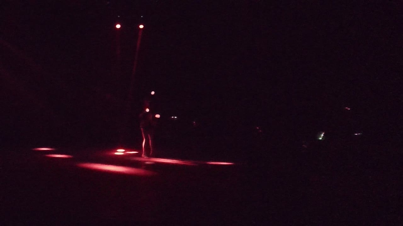 Performer centered in darkness with red light streaks on the stage floor.