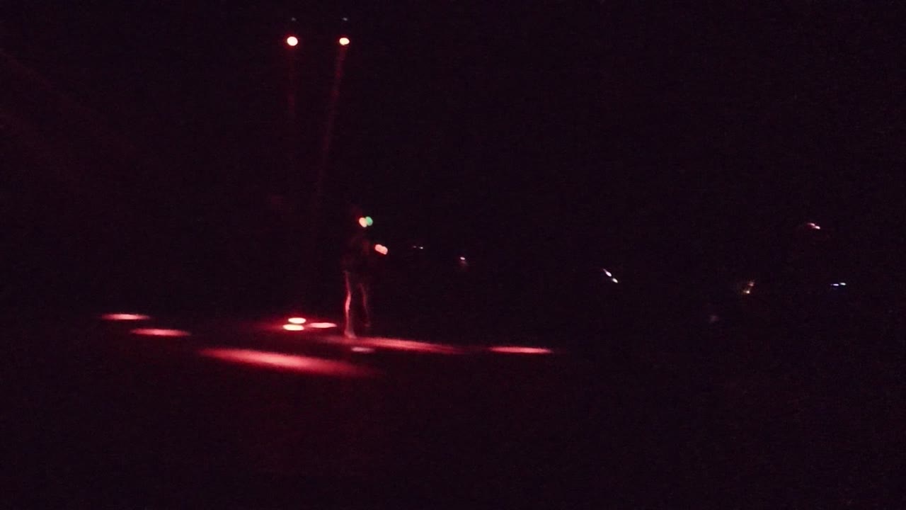 In San Jose Del Cabo, the performer shifts toward the right side of the frame as red spotlights form bright patches on the stage floor.