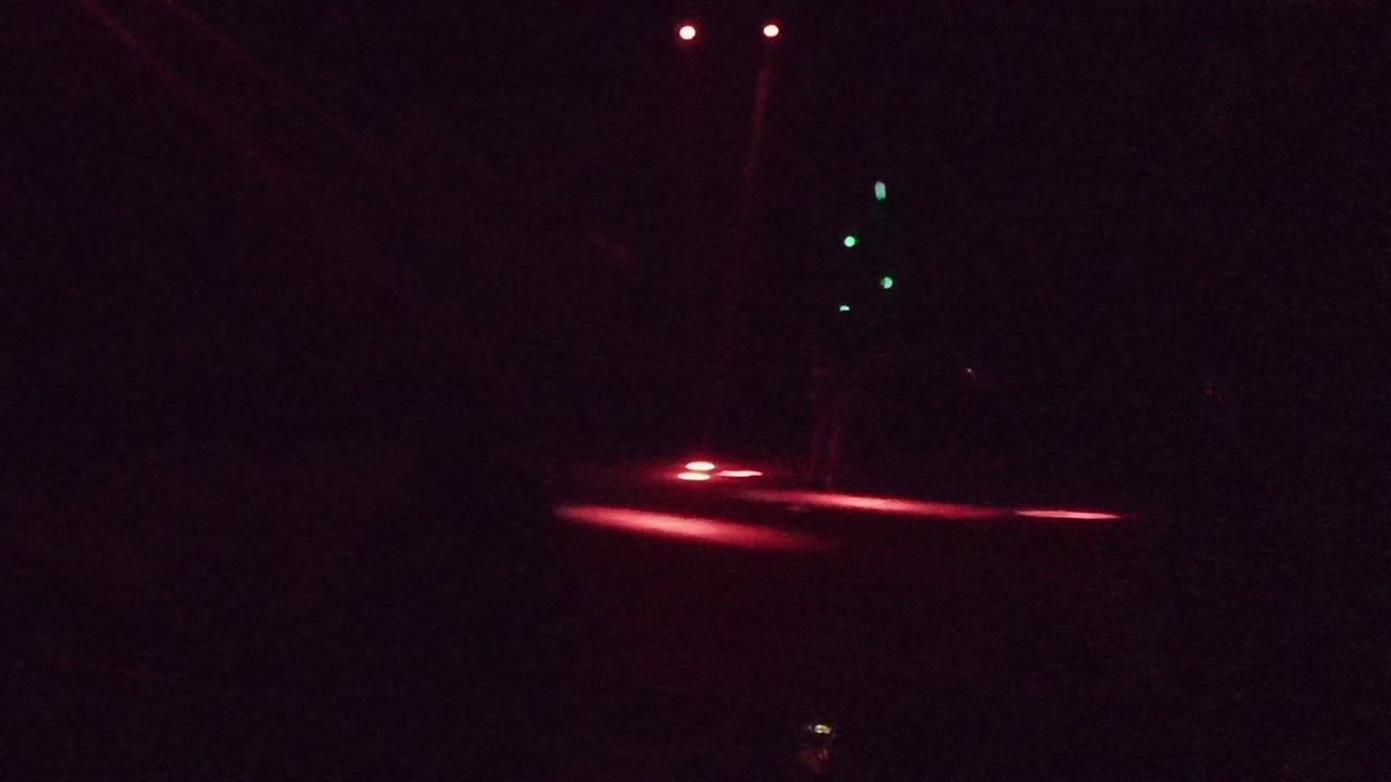 Dark San Jose del Cabo street at night with red taillight blur crossing the road and several small green traffic lights in the background.