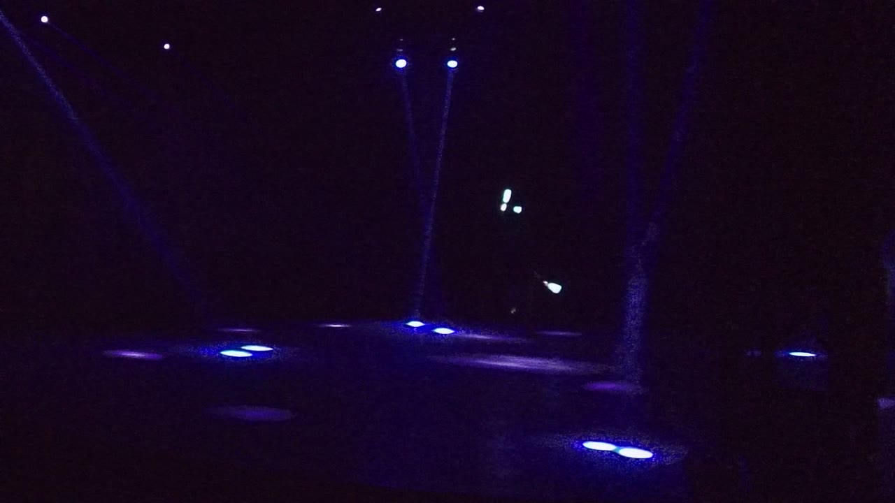 Dark outdoor pathway in San Jose del Cabo with blue ground lights across the foreground, faint overhead beams, and no visible people.