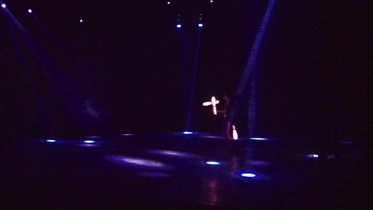 Glowing staff trails appear near center stage under blue lights.