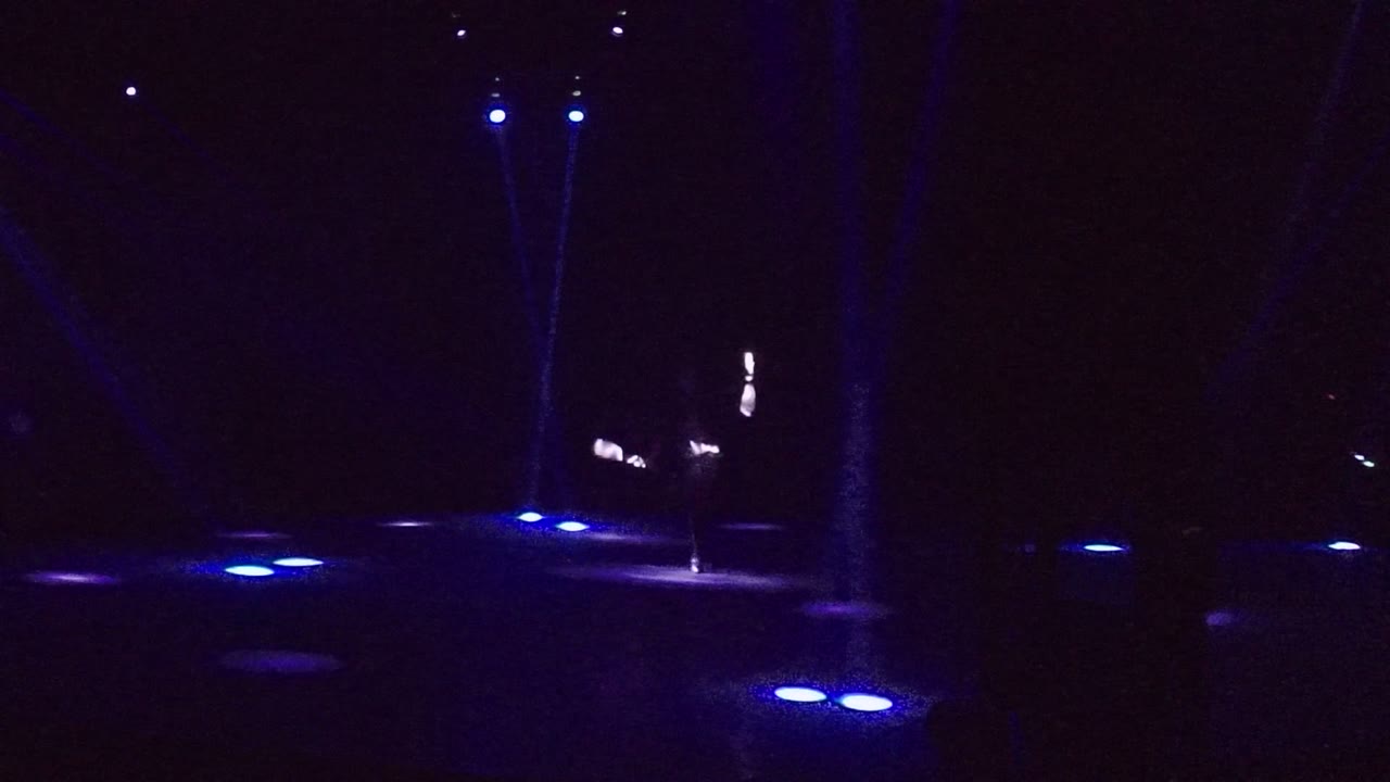Blue-lit dark stage with glowing sticks near the center.