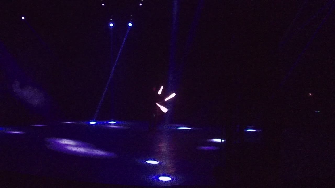 Blue-lit stage with a small cloud of haze and glowing sticks near center.
