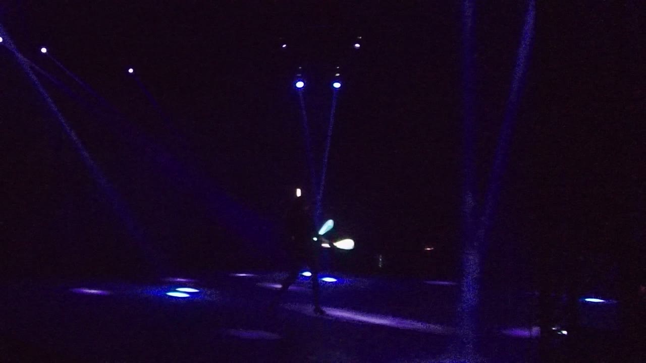 Glowing juggling props move near the center of a dark blue-lit stage.