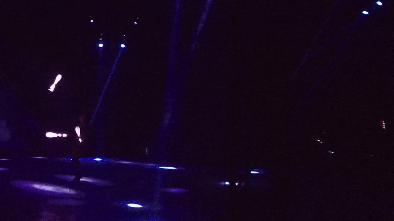 Performer silhouette crosses a blue-lit stage with a glowing staff overhead.