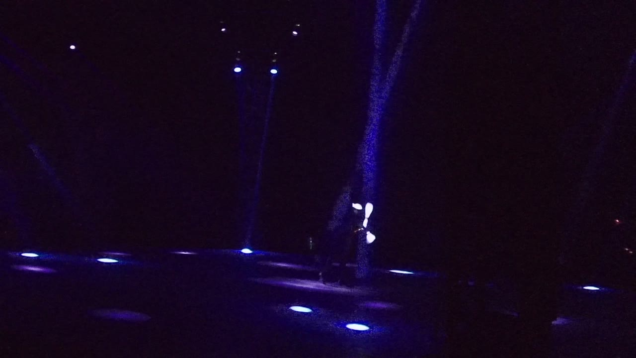 Blue-lit stage with white juggling sticks clustered near the center right.