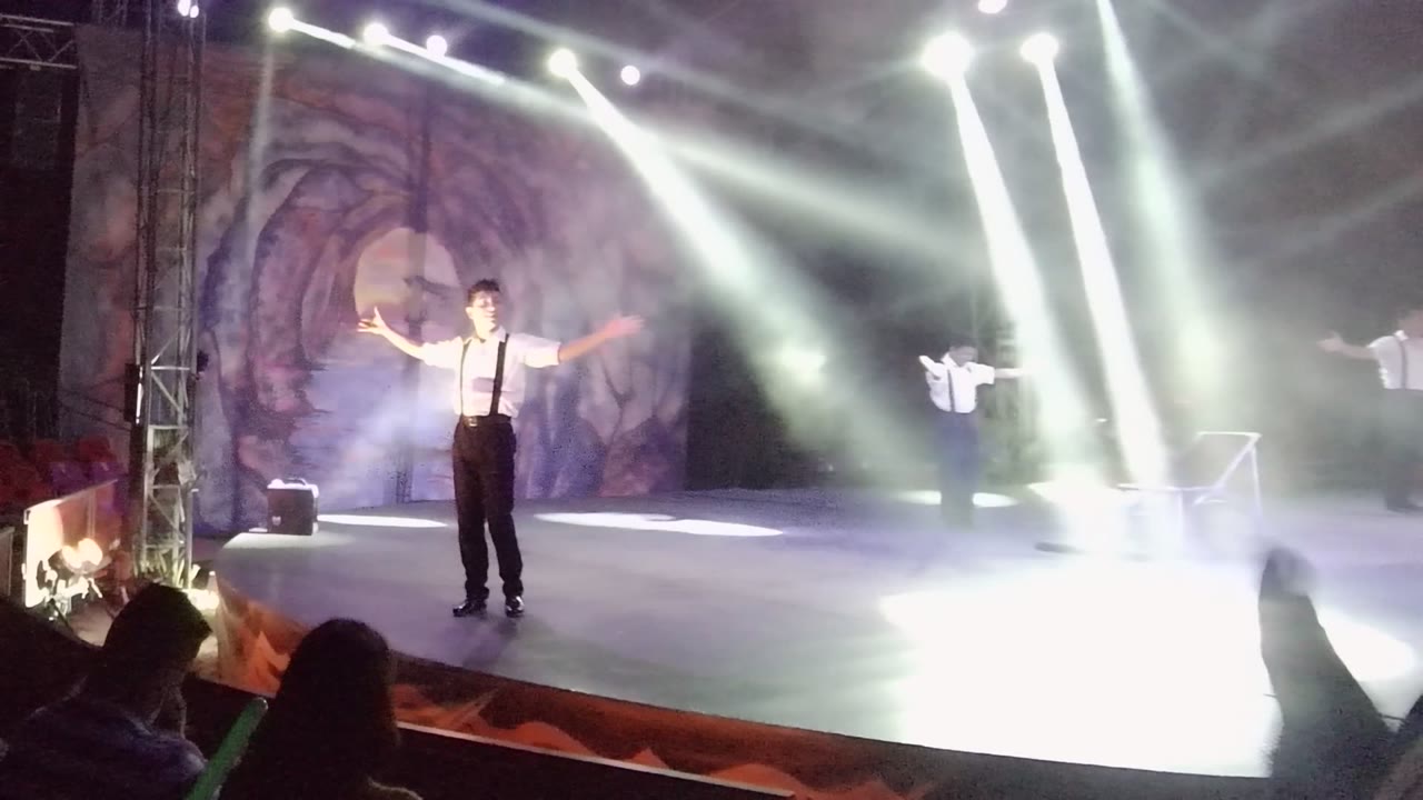 Two performers on stage under crossing white spotlights.