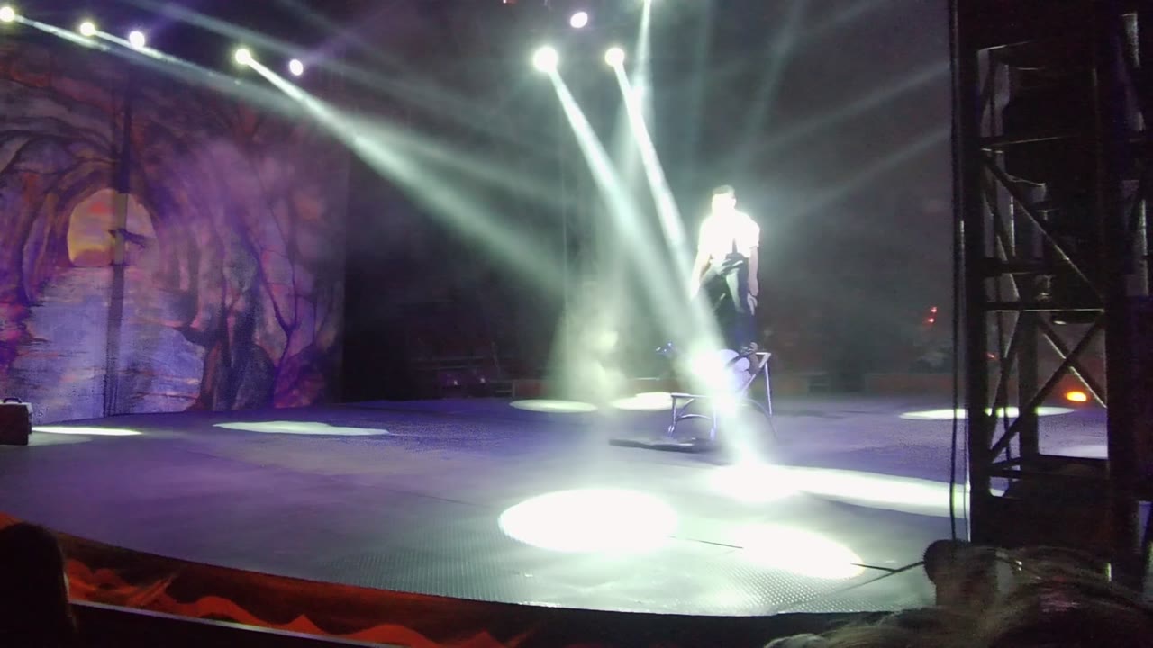 Performer stands in a spotlight beside a prop on stage.