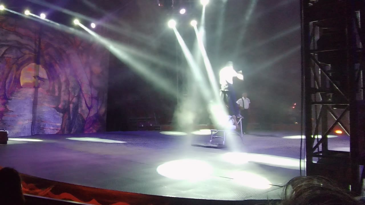 Acrobat bends forward above a supporting performer on stage.