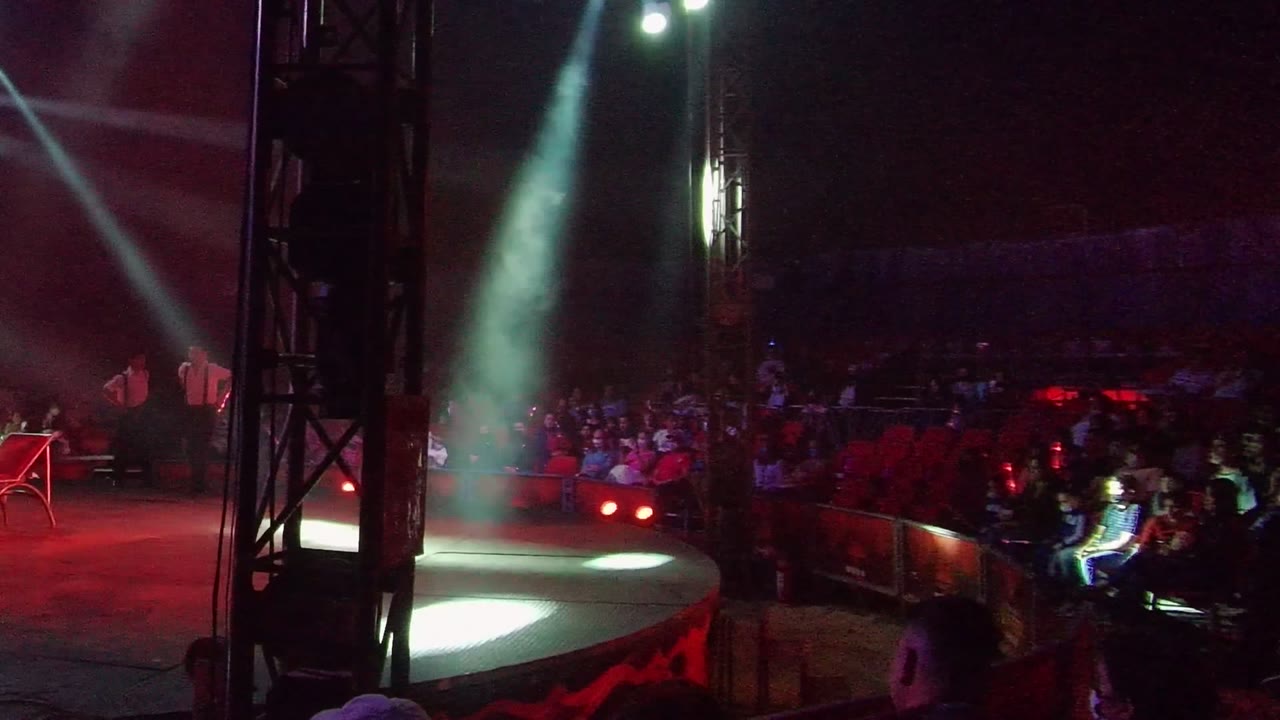 A red chair sits on the stage in San Jose del Cabo while a bright white beam cuts through haze and the audience watches from the background.