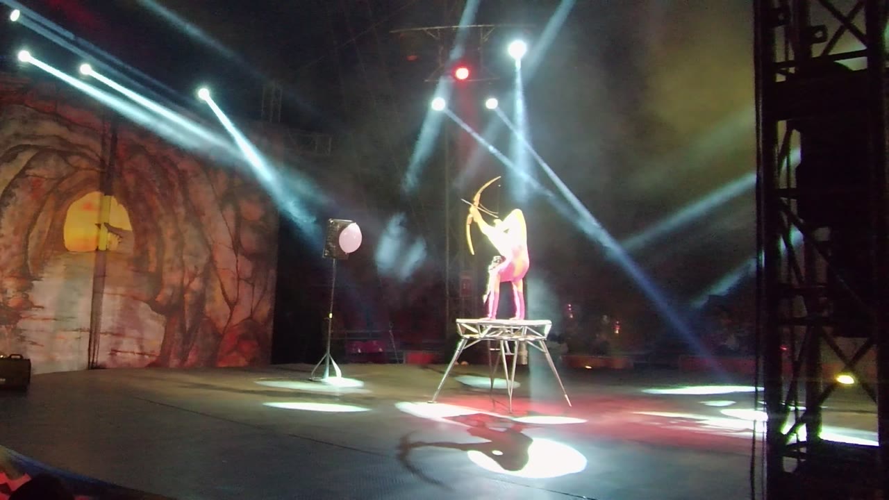 In San Jose del Cabo, Mexico, the stage archer remains on the elevated platform with crossed overhead beams, red accent lights, and a cave-themed backdrop behind.