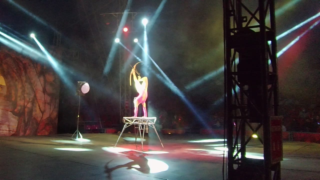 At two seconds, the performer is still lit from above on the platform, with the red ball prop left of center and the foreground rigging tower dividing the wide stage view.