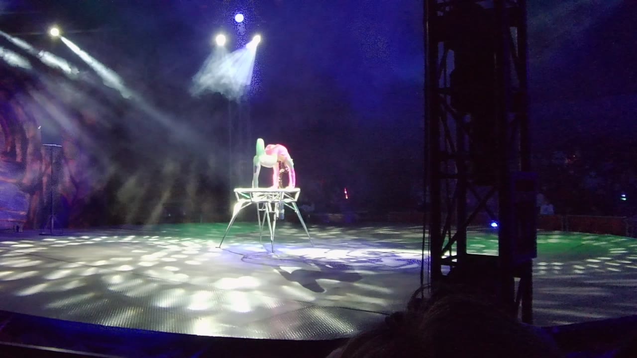 Performer balances low across a chair under bright stage lights.