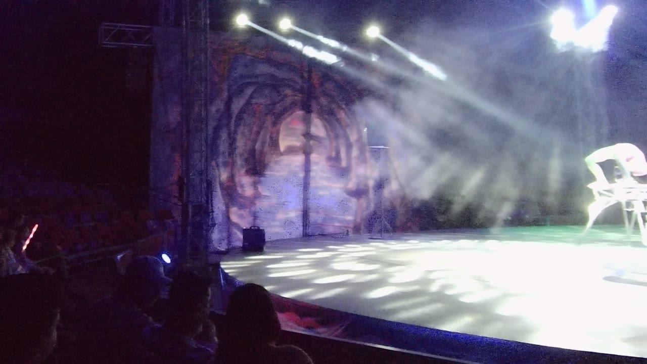 White chair near the edge of a smoky lit stage with audience silhouettes.