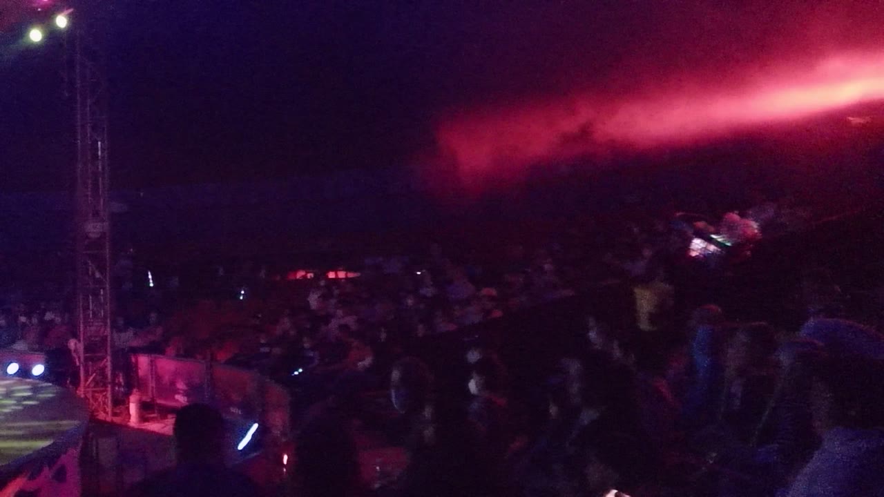 Crowd and stage edge under a red light beam with smoke overhead.