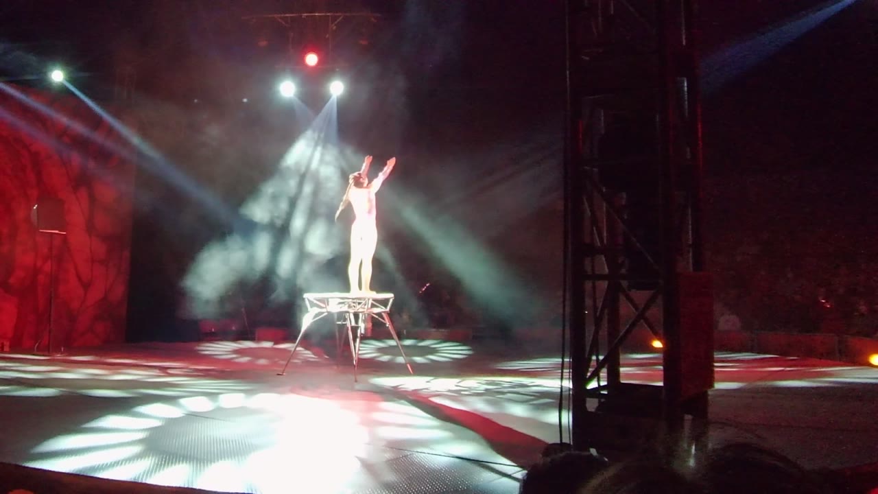 Performer in white stands on a platform with both arms raised.