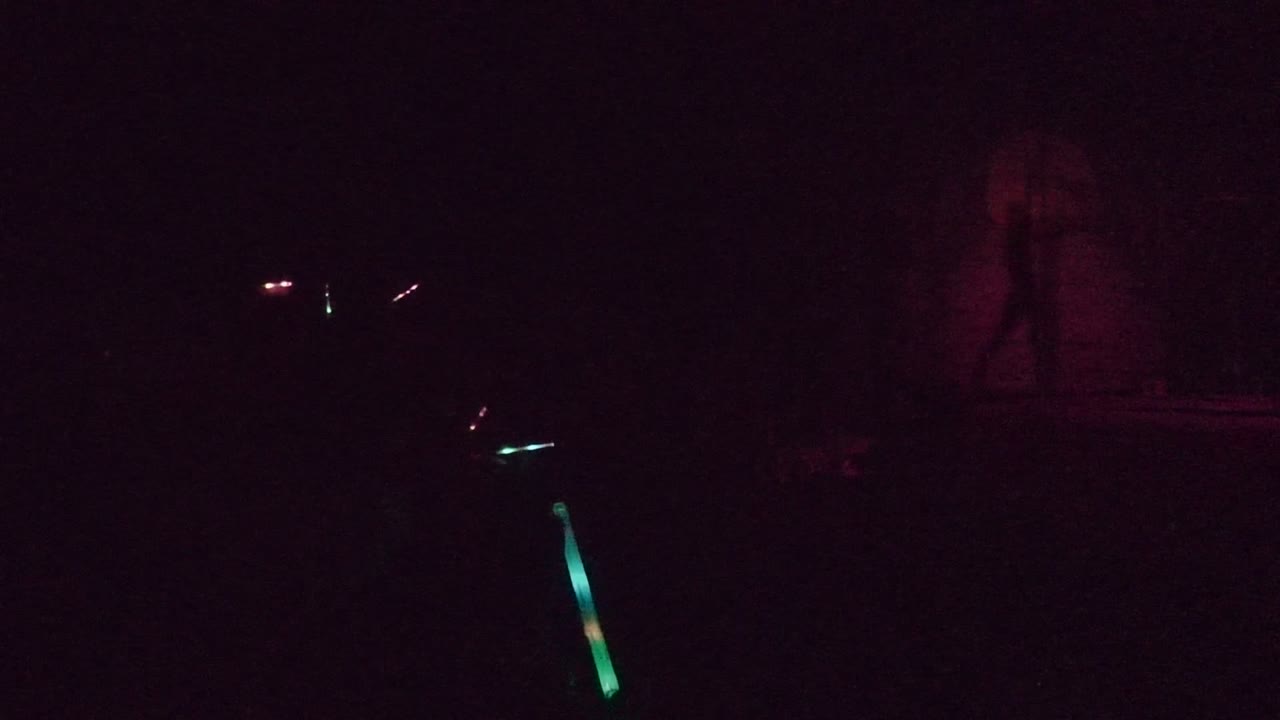 Near-dark stage in San Jose Del Cabo with faint red lighting on the backdrop and a small green light near the lower foreground.