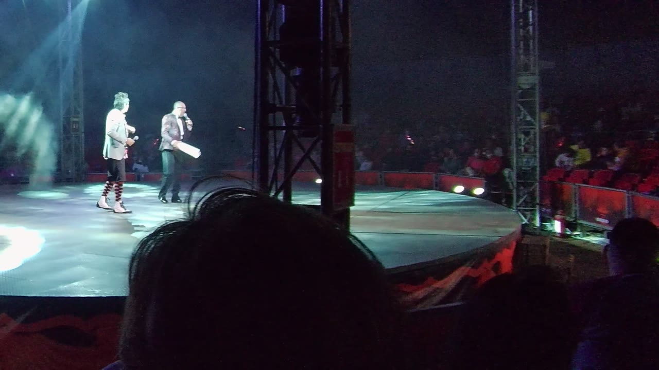 The stage edge in San Jose Del Cabo, Baja California Sur, is mostly clear of performers, with the audience in red seats, a dark foreground silhouette, floor lighting, and stage truss visible.