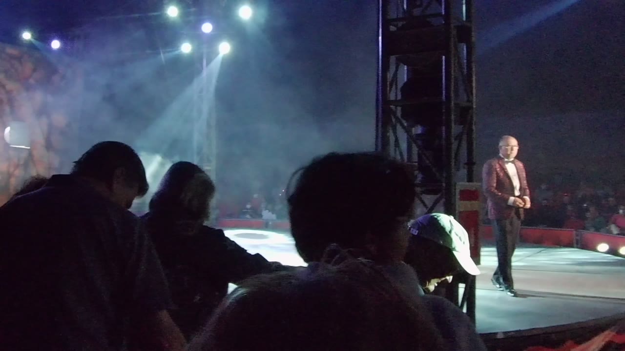 In San Jose del Cabo, a suited performer stands on a bright stage while audience silhouettes crowd the foreground under white spotlights and haze.