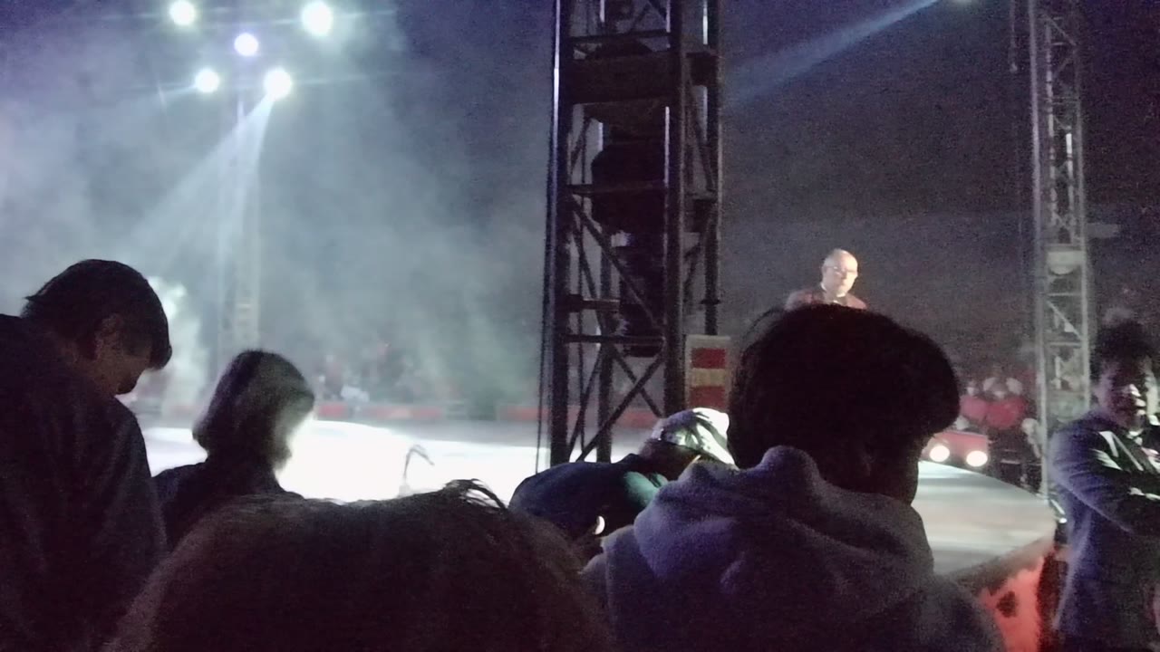 Audience members shift in front of a smoky stage with a suited performer.