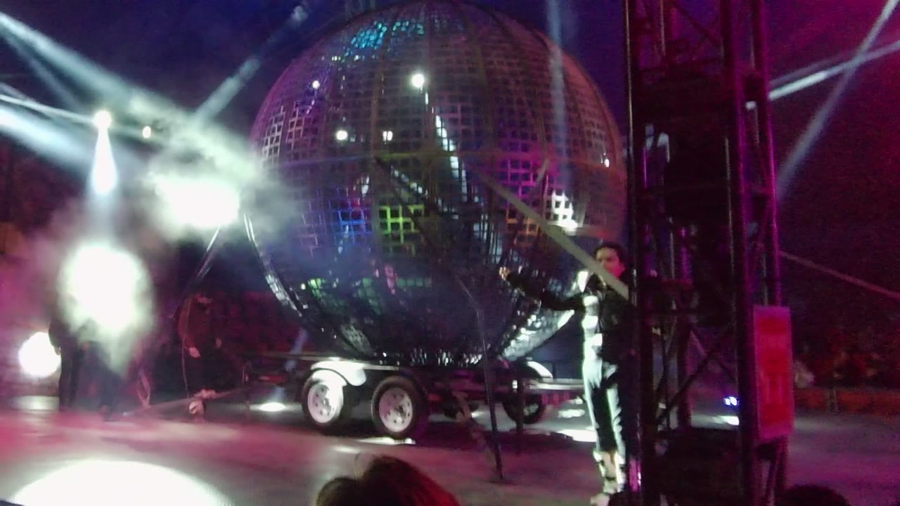 In San Jose del Cabo, a giant reflective sphere on a trailer fills the stage as performers stand nearby under bright white beams and magenta lighting.