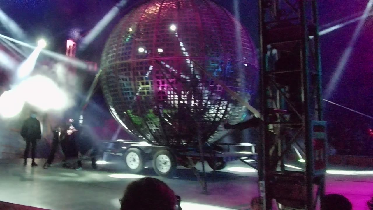 Large mirrored sphere on stage with performers partly silhouetted by bright lights.