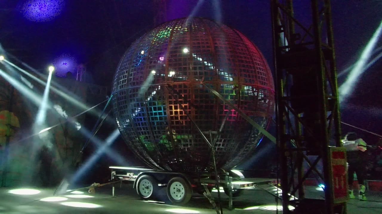Illuminated sphere on stage with white beams crossing through smoke.