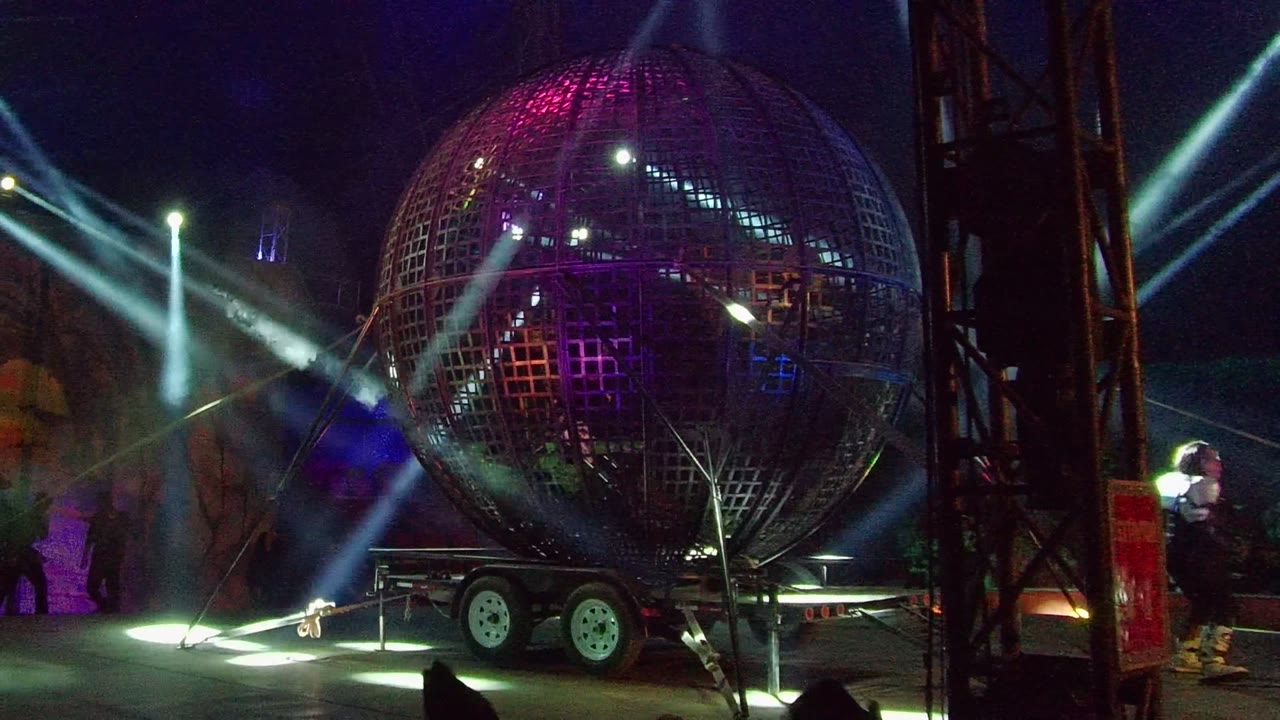 A reflective grid sphere fills the right side of the San Jose Del Cabo stage frame, with trailer wheels below, white beams overhead, and a person visible near the right edge.