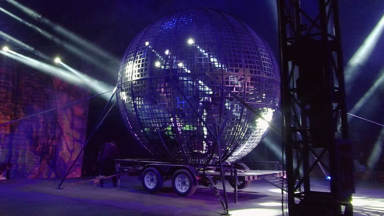 Illuminated sphere on trailer with beams and dark stage structure