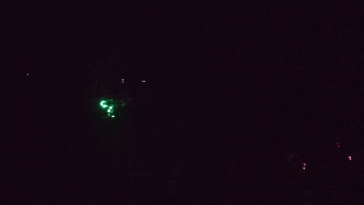 Very dark opening frame from San Jose Del Cabo with scattered green lights and only faint outlines of the performance structure, no visible people.