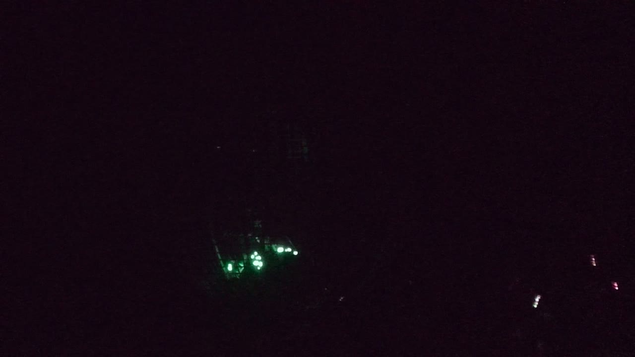 The San Jose Del Cabo performance cage fills the frame with white spotlights crossing above it, green lights glowing inside, and a performer partly visible near the right edge.