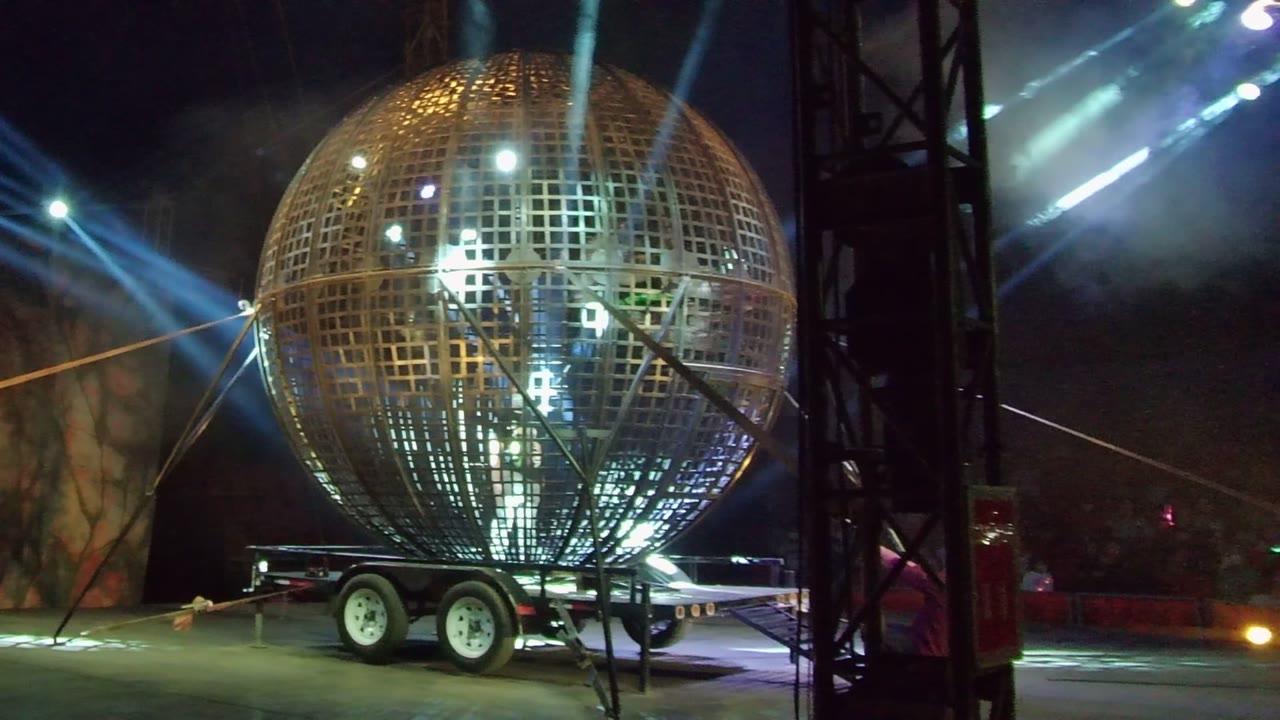 Large golden sphere on a trailer in San Jose Del Cabo, Baja California Sur, with stronger blue beams across the smoky background and no visible people.