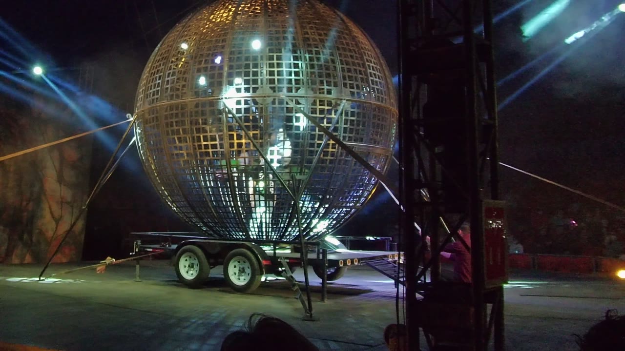 Grid sphere on trailer with bright interior lights and stage beams.