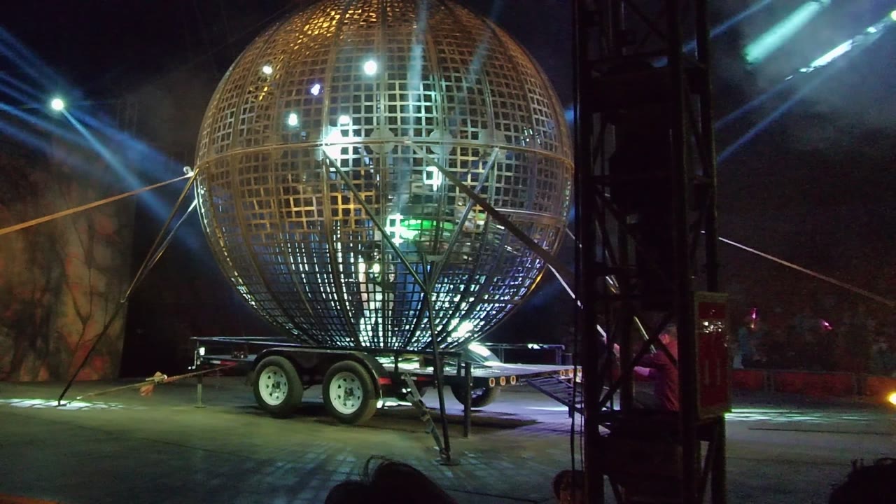 A green glow appears inside the large grid sphere in San Jose del Cabo, while blue stage lights and a dark vertical truss frame the night scene.
