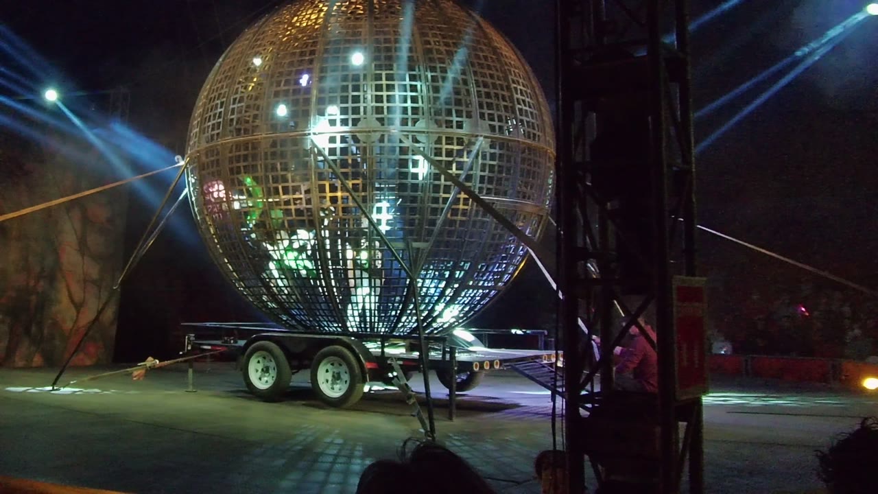 San Jose del Cabo nighttime stage frame with the metallic sphere centered over the trailer, crossed by blue spotlight beams and a thin amber beam in the background.