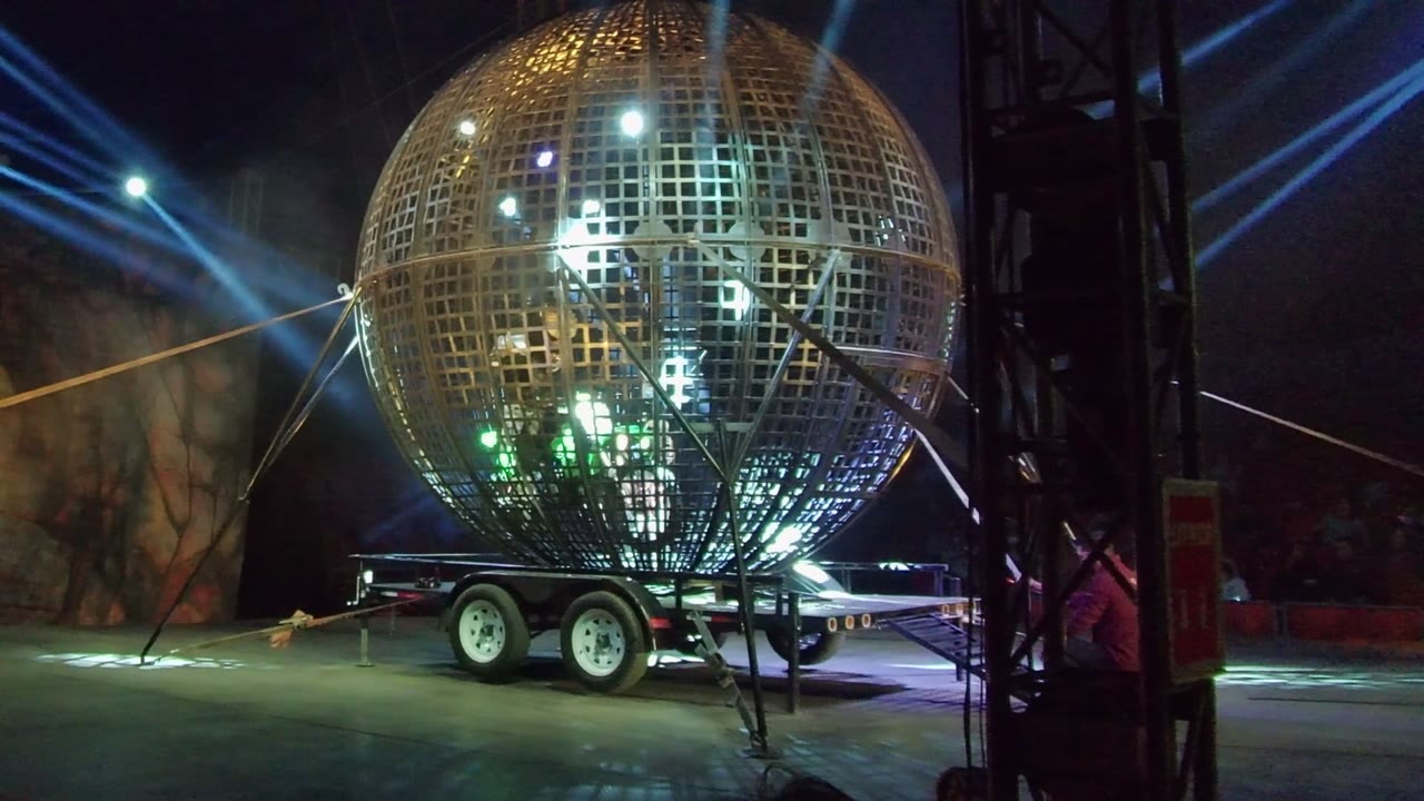 Grid sphere lit with white and green patterns beside stage truss