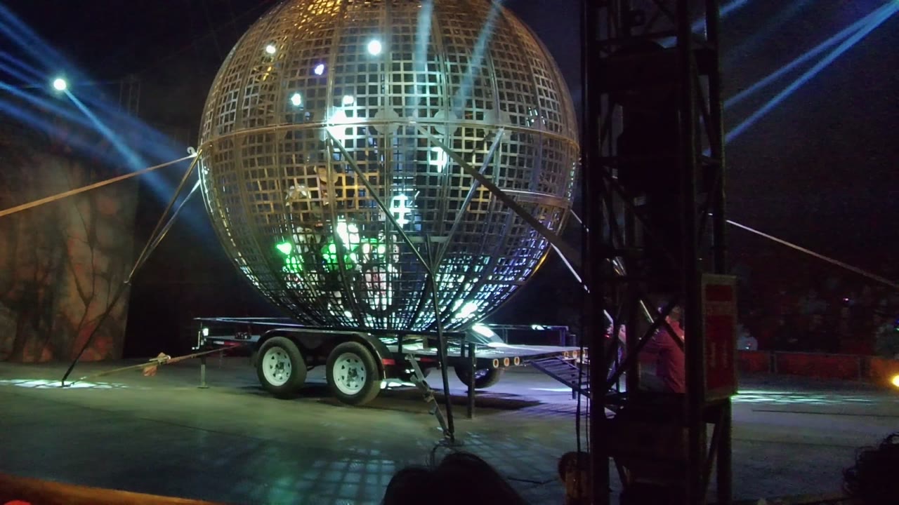 Reflective sphere and trailer lit by blue beams and white spotlights