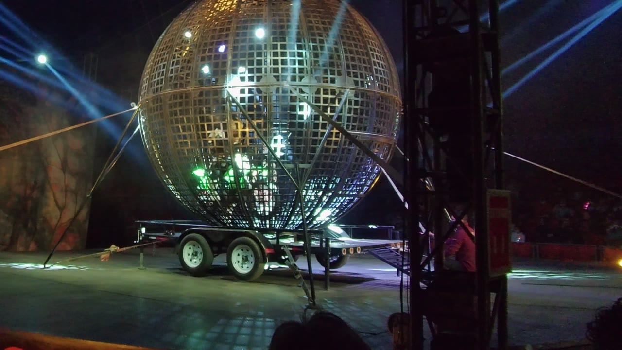A stage-lit metallic sphere on a wheeled trailer fills the right side of the San Jose Del Cabo frame, with vertical rigging in front and colored lights reflecting from the grid surface.