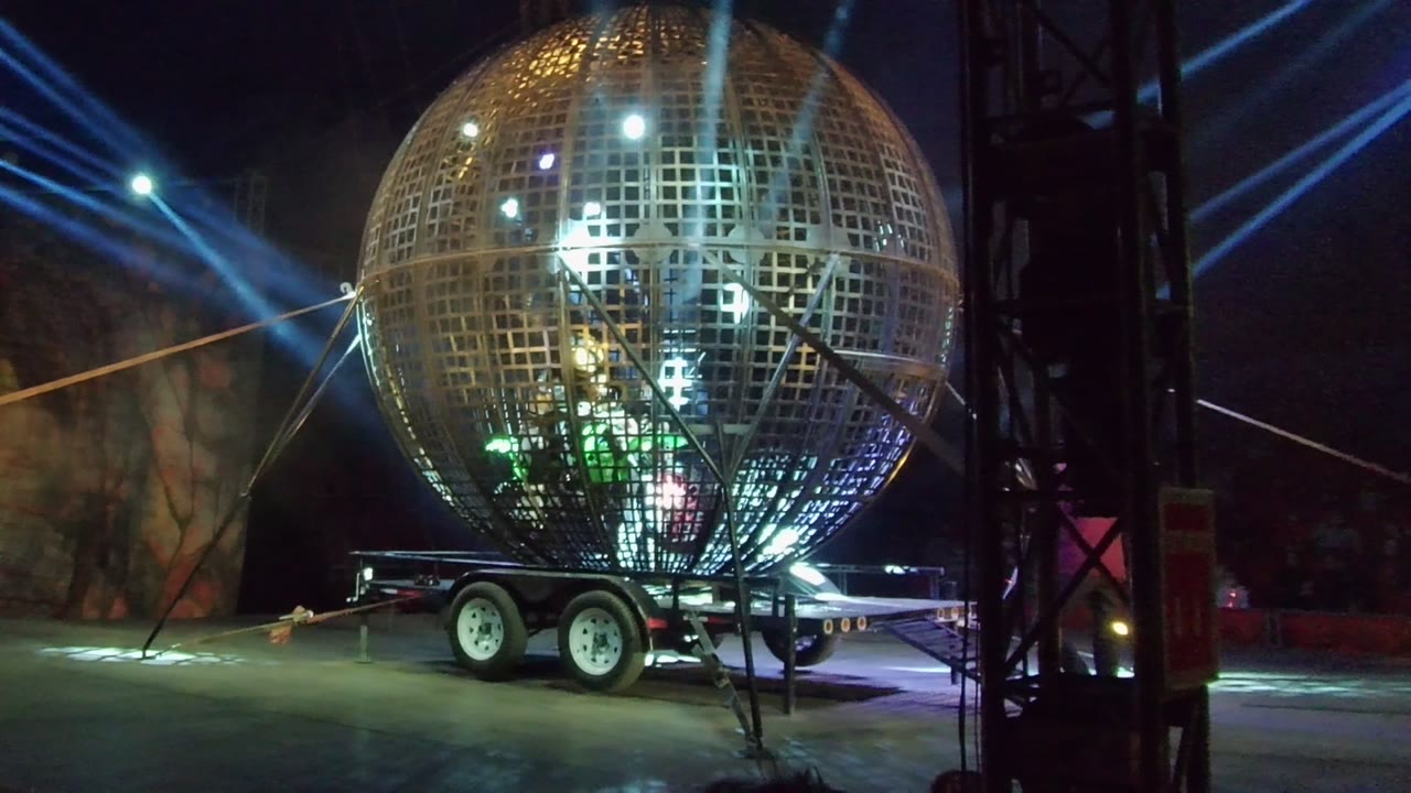 Trailer-mounted spherical light structure with blue beams across a dark background.