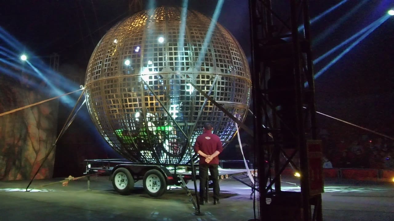 Shiny sphere mounted on a wheeled trailer under crossing blue lights