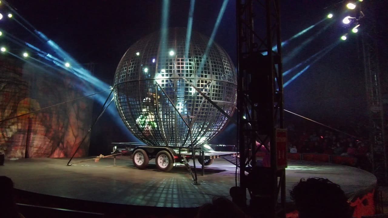 Metal sphere stage prop with green light and spotlights crossing above.