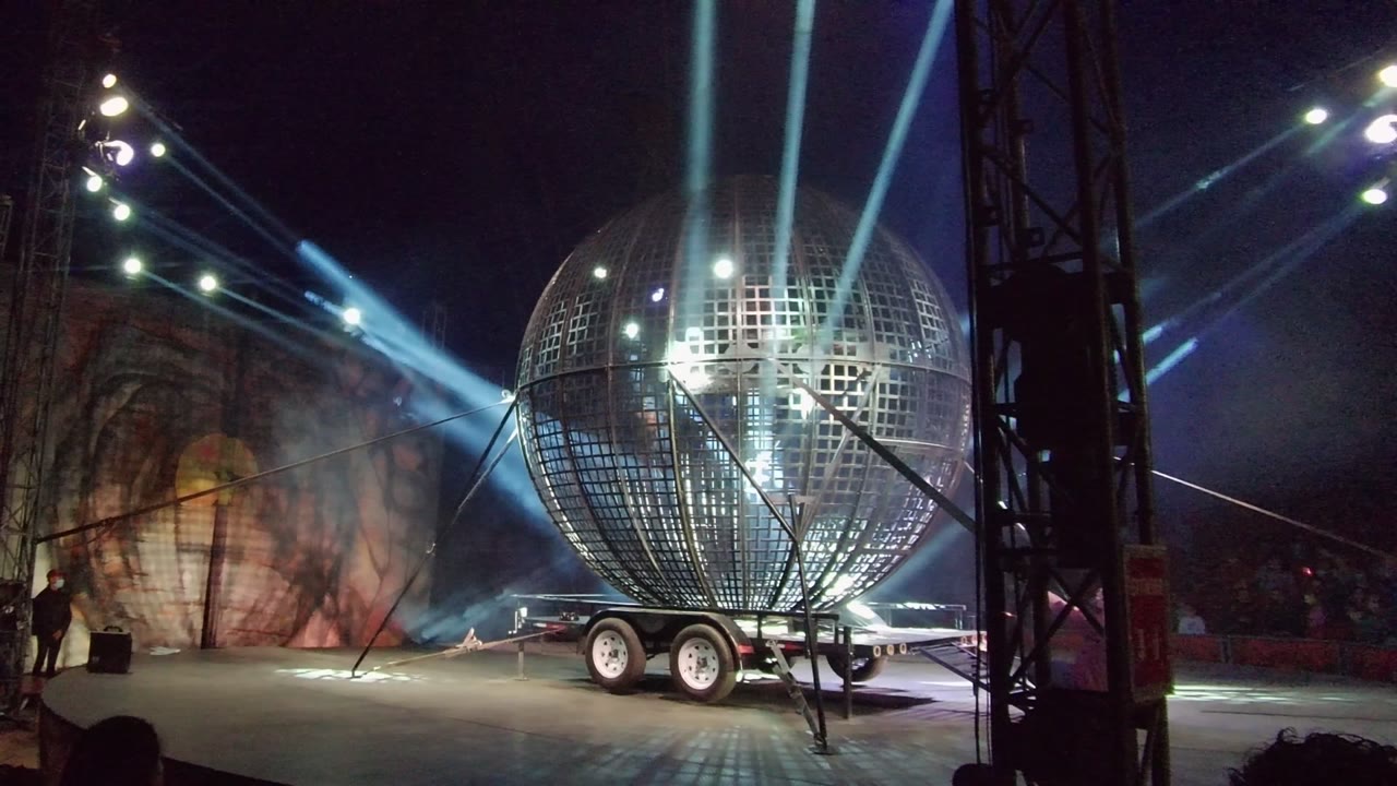 Stage sphere and trailer lit by crossing blue beams.