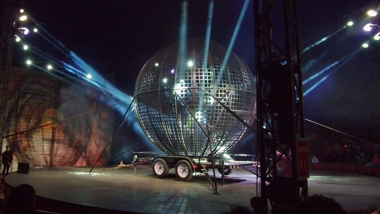 Reflective metal globe on trailer with a person near the stage backdrop.