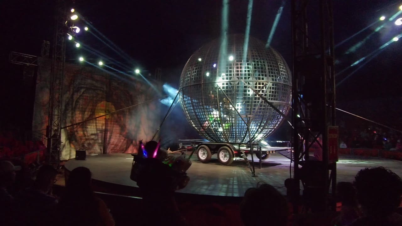 Disco ball stage lit by beams with a performer near the foreground.