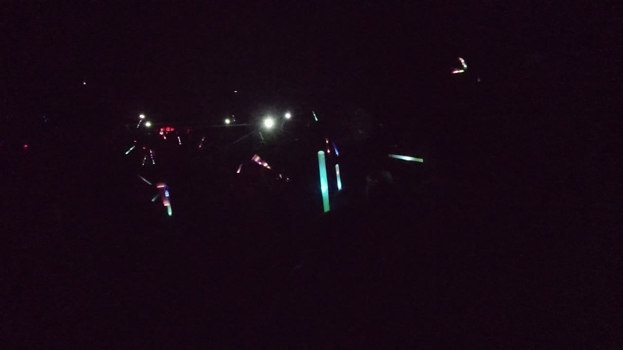Dark San Jose del Cabo nighttime event frame with scattered green, blue, red, and white lights across a shadowed crowd area.