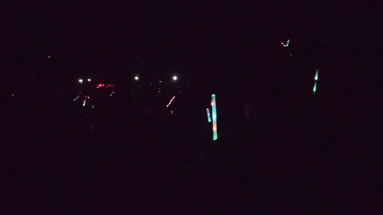 Mostly dark frame with bright glow sticks and distant light points.