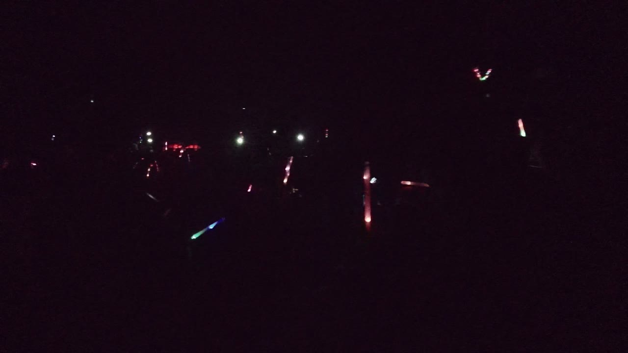 Dark San Jose del Cabo event frame with scattered colored glow sticks, small white lights, and a largely obscured crowd in the foreground.